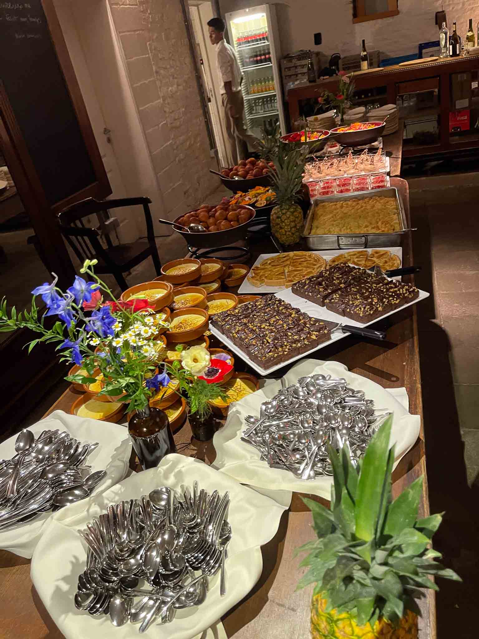 Tafel vol met gebak, taartjes, mousse, ananas en bloemen.