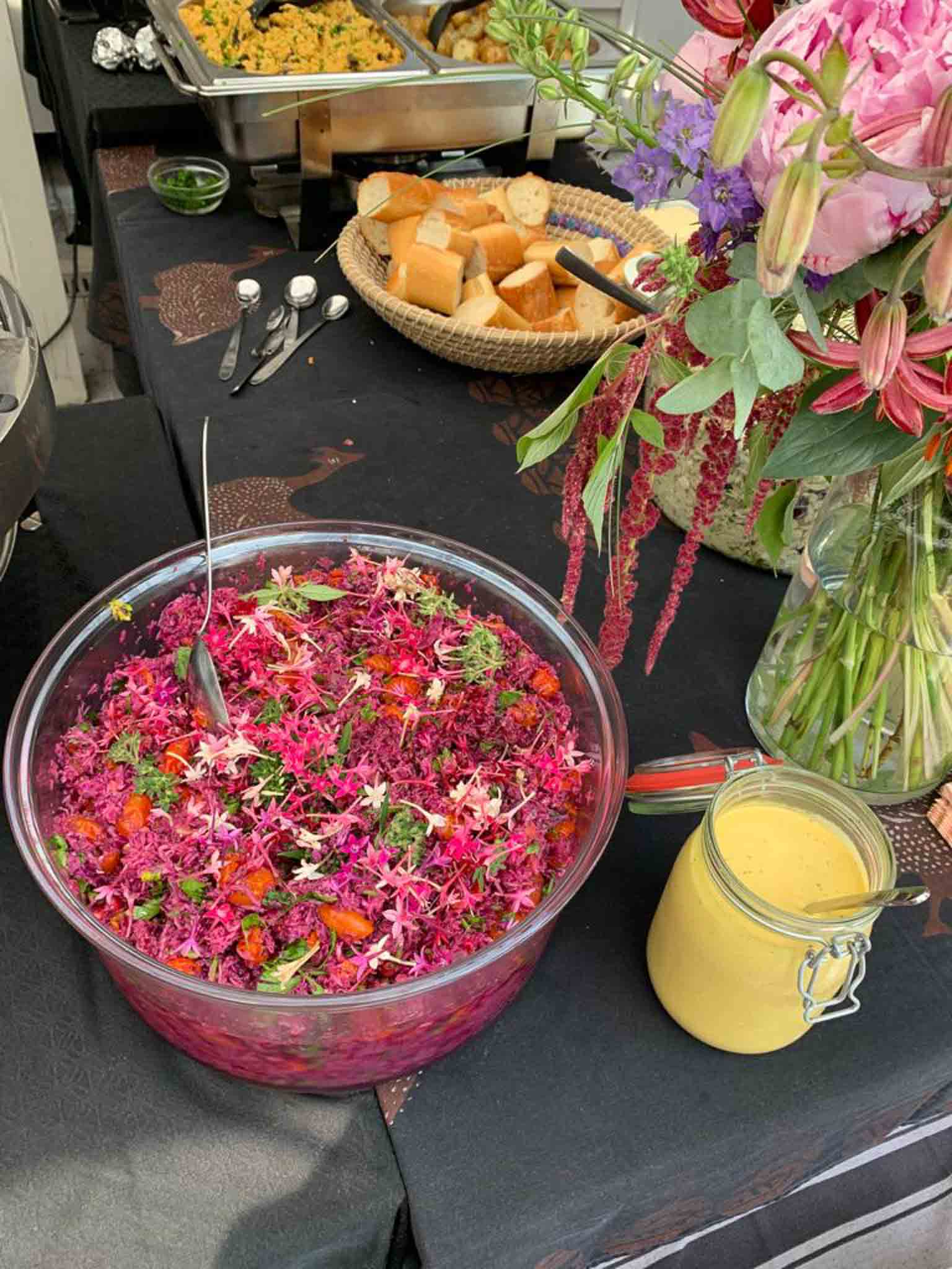 Een grote kom met roze zomersalade. Dit bestaat uit rode biet, wortel, appel en peer. Daarnaast citroencrème en daarboven een broodmand.